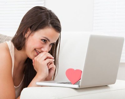 woman smiling at laptop, which has a heart resting on it as illustration for Why Writing an Online Dating Profile Well is Essential